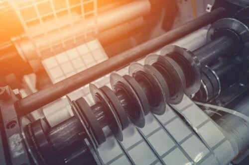 Rotating knives for cutting a self-adhesive label into several narrow ribbons. Equipment for the production of self-adhesive labels. Rotary die cutting machine with slitting blade. Selective focus.